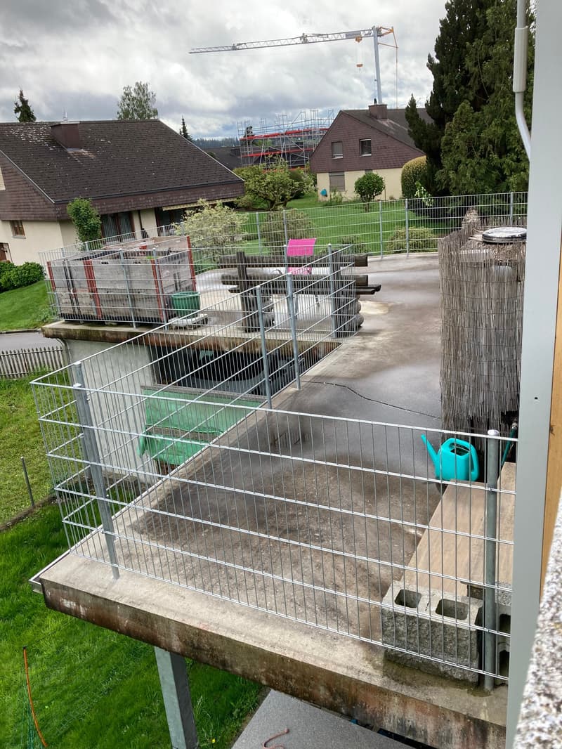 Balcony with metal railing, concrete floor, and a small green watering can placed on the edge.