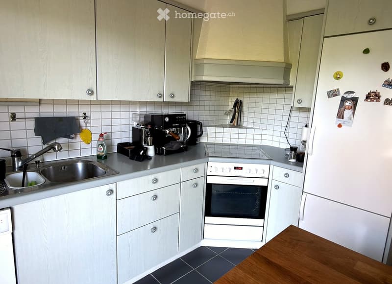 Modern kitchen with white cabinets, stainless steel sink, coffee maker, oven, and refrigerator. The countertops are gray, and the floor is tiled.