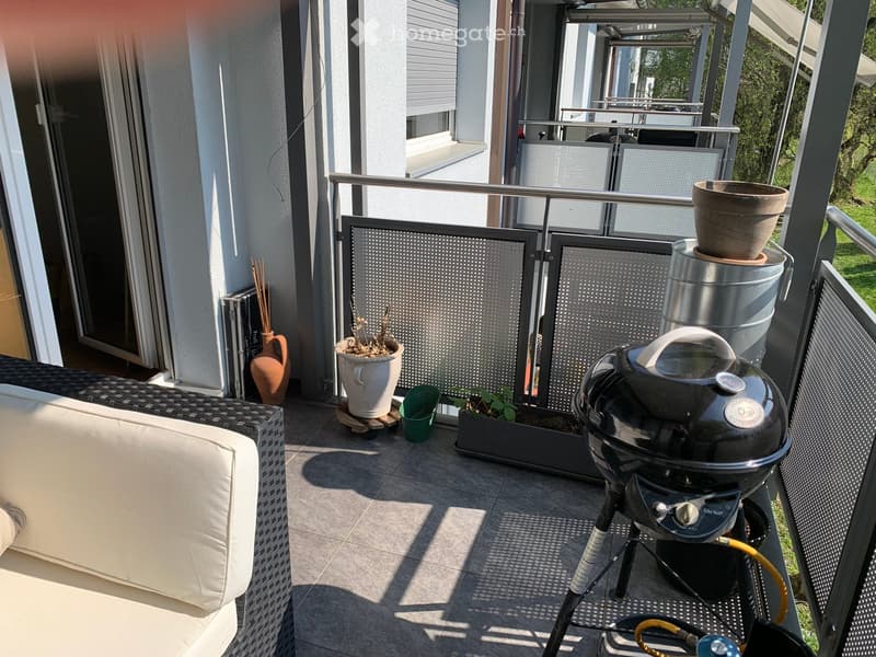 Balcony with a white wicker sofa, a black barbecue, several potted plants, and decorative vases.