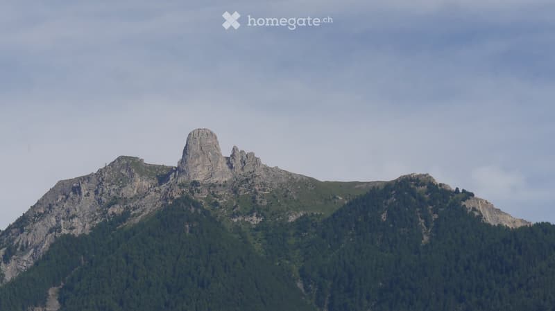 A mountain range with rocky peaks and dense forest cover, under a partly cloudy sky.