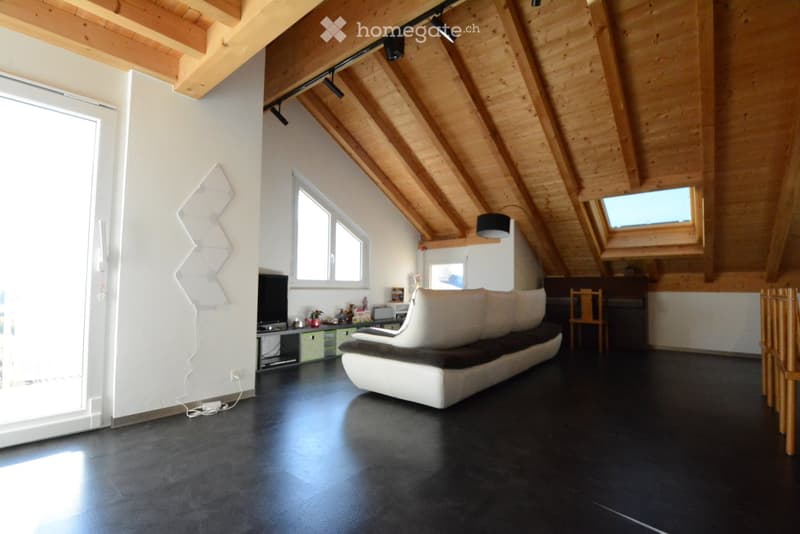 Modern living room with exposed wooden beams, large windows, and skylights. Features a white sectional sofa, a wooden chair, a small table, and a television on a stand.