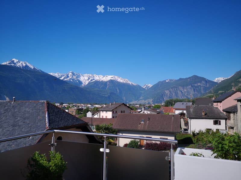 Balcony overlooking a town with houses and snow-capped mountains in the background.