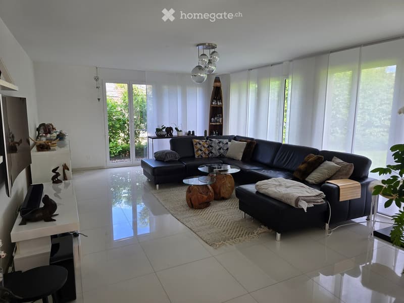 Modern living room with a black leather sectional sofa, glass coffee table, wooden stools, and a large window with sheer curtains.