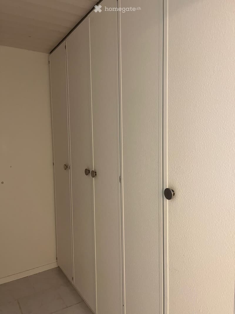 Empty hallway with beige walls, tiled floor, and closed doors with silver handles.