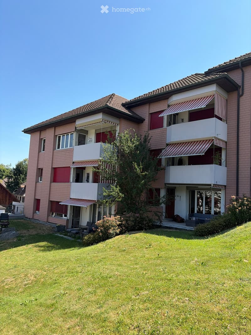 Two-story house with pink brick exterior, multiple balconies with striped awnings, and a well-maintained lawn in front.