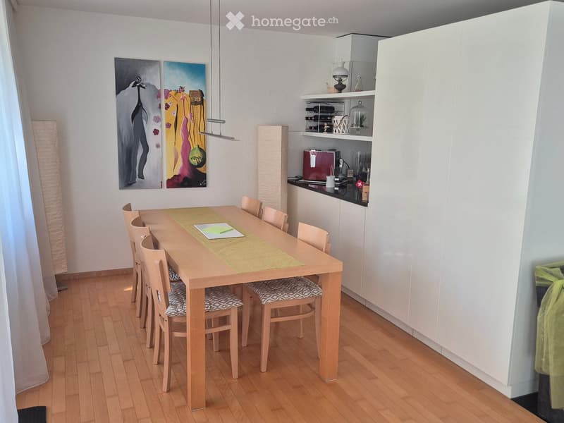 Dining area with a wooden dining table, six chairs, and a modern kitchen cabinet with shelves and appliances.