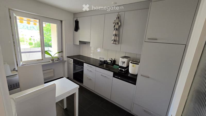 Modern kitchen with white cabinets, black countertops, and stainless steel appliances. Includes a small dining area with a white table and chairs, a coffee maker, and a toaster on the counter.