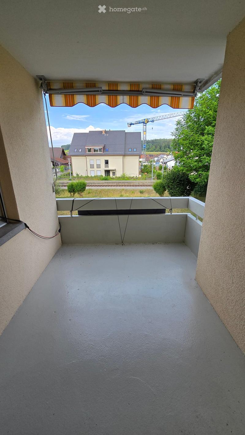 Empty balcony with white railing, striped awning, and view of residential area and construction crane.
