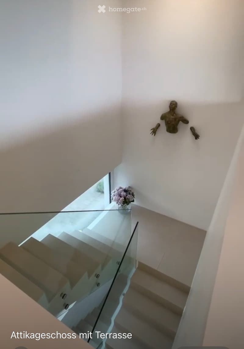 Modern glass staircase leading to an attic level with a visible terrace, white walls, and a decorative sculpture on the wall.