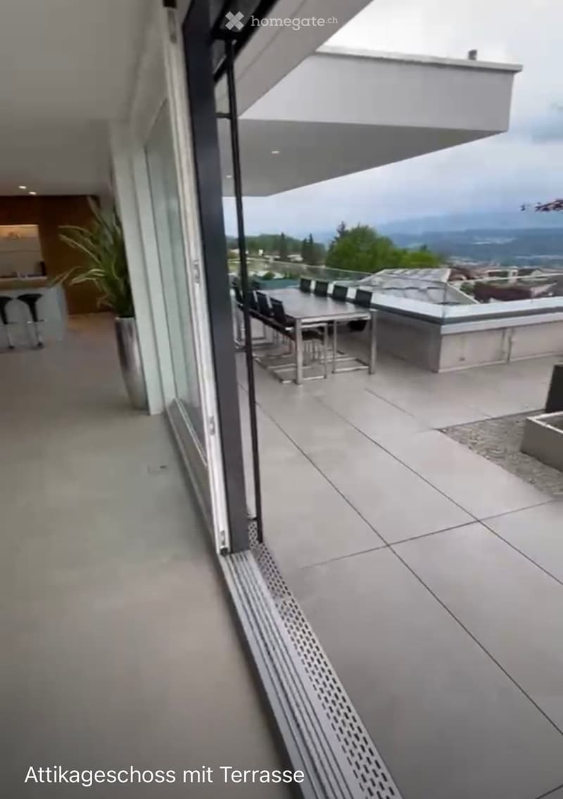 Modern rooftop terrace with a view of the city and mountains, featuring a dining table and chairs.