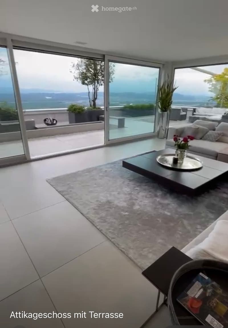 Modern living room with large windows offering a scenic view, featuring a sofa, coffee table, side table, and decorative vase.
