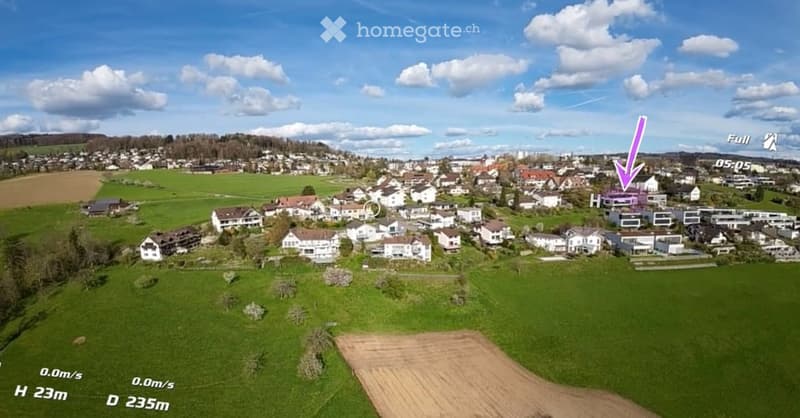 Aerial view of a residential neighborhood with multiple houses, green fields, and a clear blue sky.