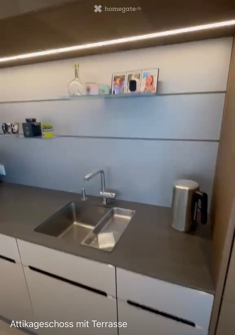 Modern kitchen with light grey cabinets, stainless steel sink, and countertop. Includes a cup, vase, and picture frames on the counter.
