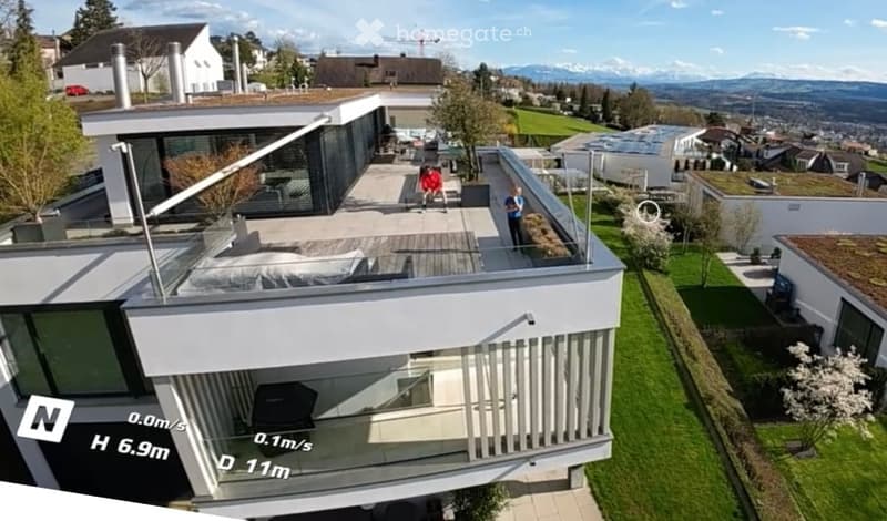 Modern two-story house with a flat roof, large windows, and a spacious rooftop terrace overlooking a scenic landscape with mountains in the background.