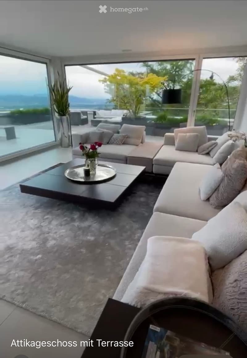 Modern living room with large windows offering a scenic view, featuring a sectional sofa, coffee table, and decorative vase with flowers.