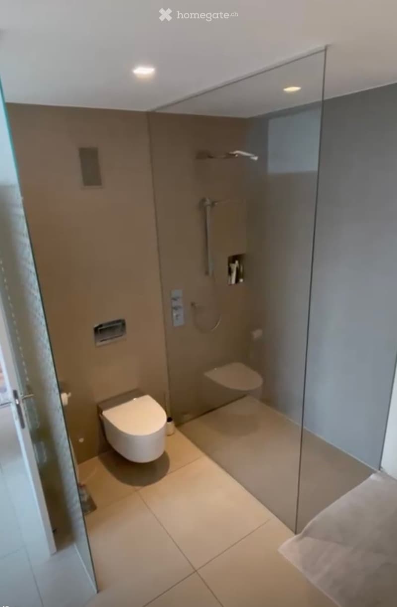 Modern bathroom with a toilet, glass-enclosed shower stall, and tiled floor.