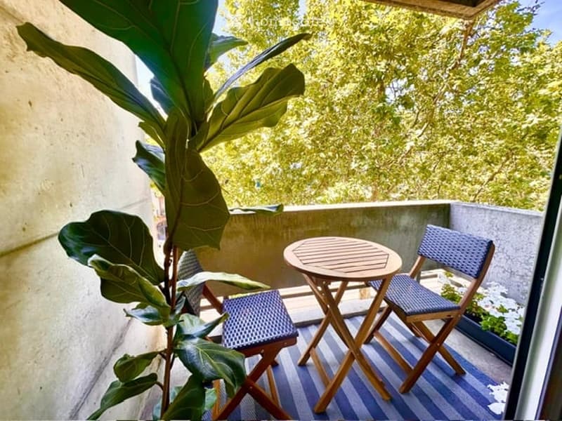Balcony with a small round table and two folding chairs, a large leafy plant, and a blue and white striped rug.