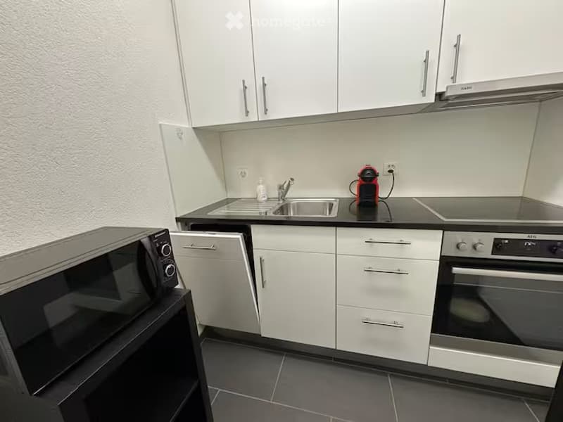 Modern kitchen with white cabinets, black countertops, stainless steel appliances including a microwave, oven, and coffee maker, and a sink with a faucet.