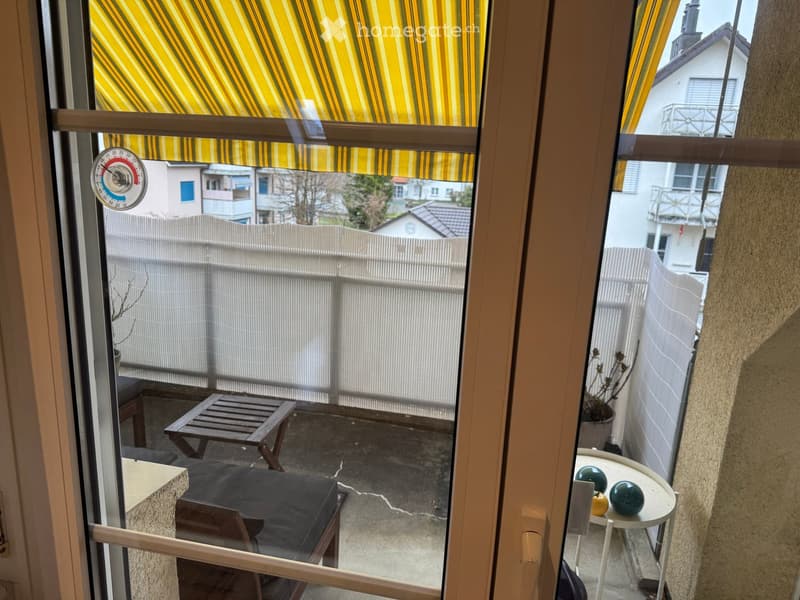Balcony with a small table, chairs, and decorative balls, overlooking a fenced yard with neighboring houses.