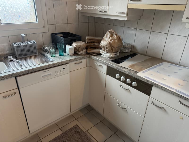 Modern kitchen with white cabinets, granite countertops, and stainless steel appliances including a dishwasher and oven. Various kitchen items are placed on the countertops.