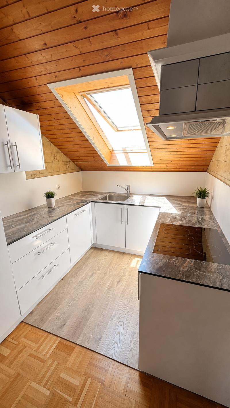 Modern kitchen with white cabinets, wooden flooring, marble countertops, and a skylight window above the sink.