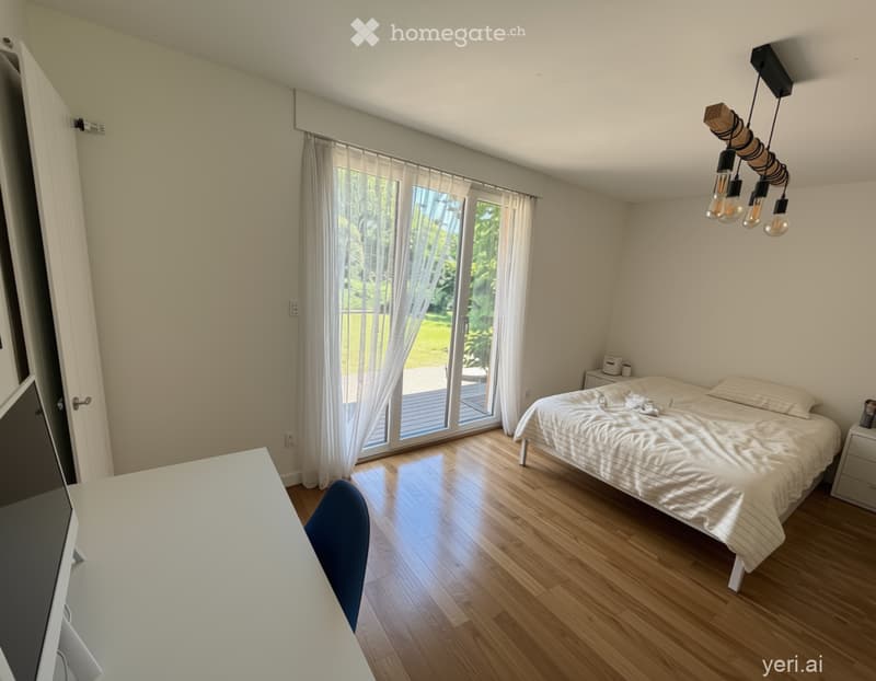 Bright bedroom with wooden flooring, large window with white curtains, bed with white bedding, a blue chair, a white table, and a modern light fixture.