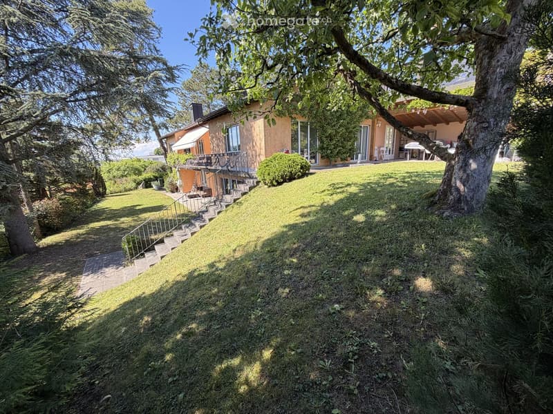 A well-maintained garden with a lawn, trees, and a house with a balcony and patio area.