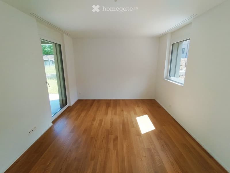 Empty room with wooden flooring, white walls, large window, and glass sliding door leading outside.