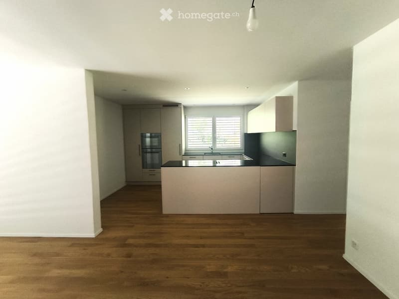 Modern kitchen with light-colored cabinets, a central island, and a dark countertop. The space features wooden flooring and large windows with blinds.