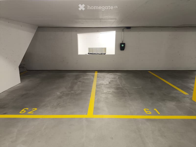 Underground parking space with concrete floor, yellow parking lines, and numbered spots61 and 62. A small window at the far end provides natural light.