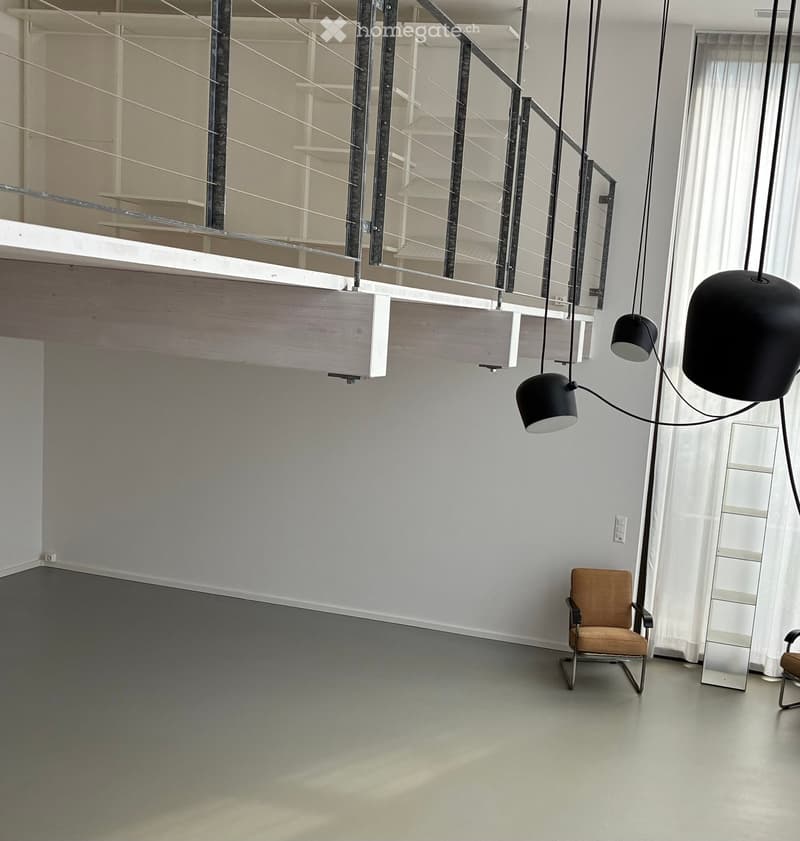 Open-plan space with two modern chairs, pendant lights, and a glass balcony overlooking the room.