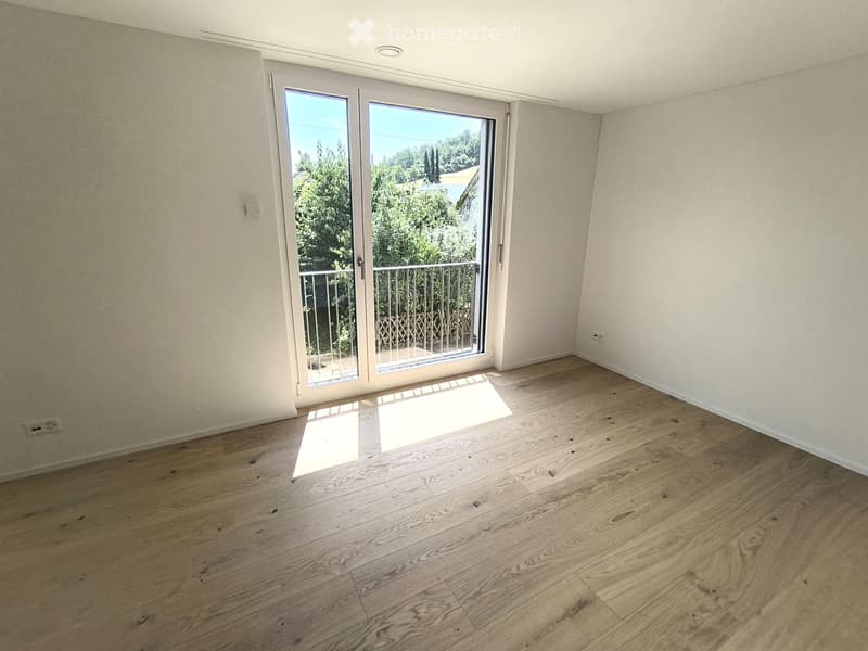 Empty room with wooden flooring, white walls, and a large sliding glass door leading to a balcony with a metal railing.