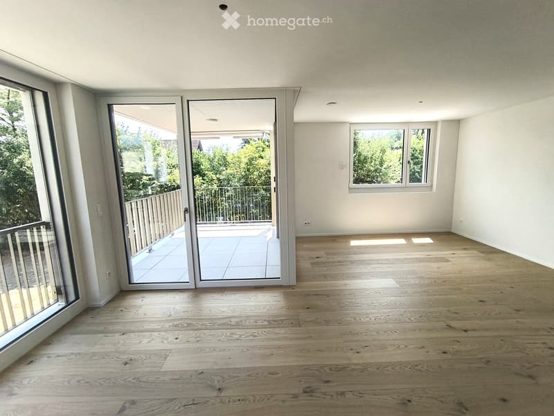 Empty room with light wooden flooring, large windows, and sliding glass doors leading to a balcony.