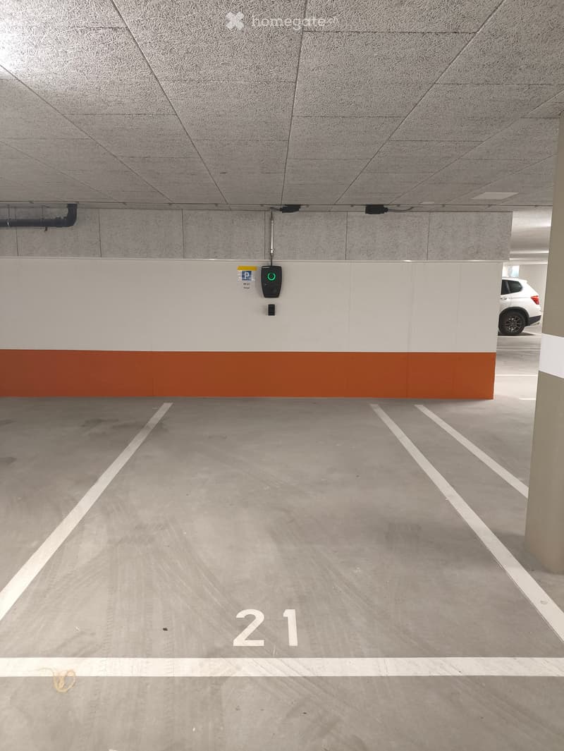 Underground parking area with marked parking spaces, concrete pillars, and a charging station for electric vehicles.