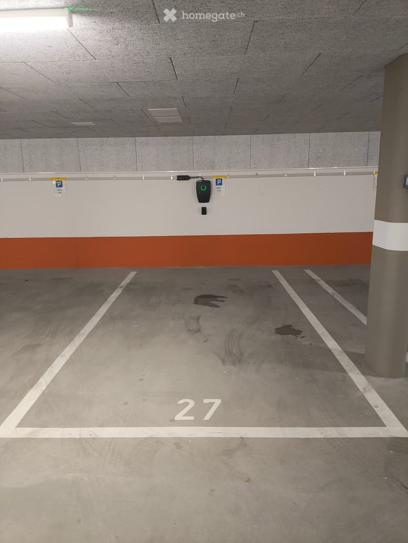 Empty underground parking space with marked parking spots, white lines, and a digital parking system display on the wall.