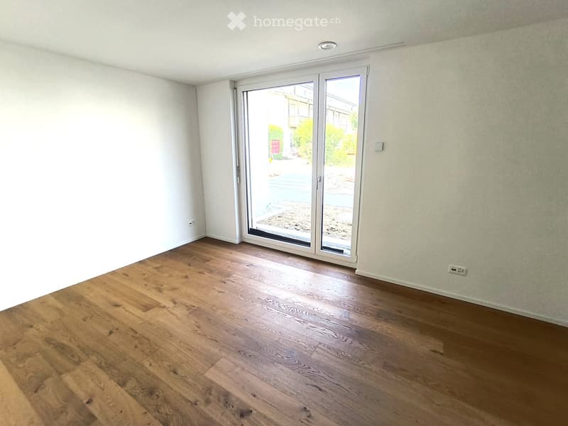 Empty room with wooden flooring, white walls, and large sliding glass doors leading to an outdoor area.