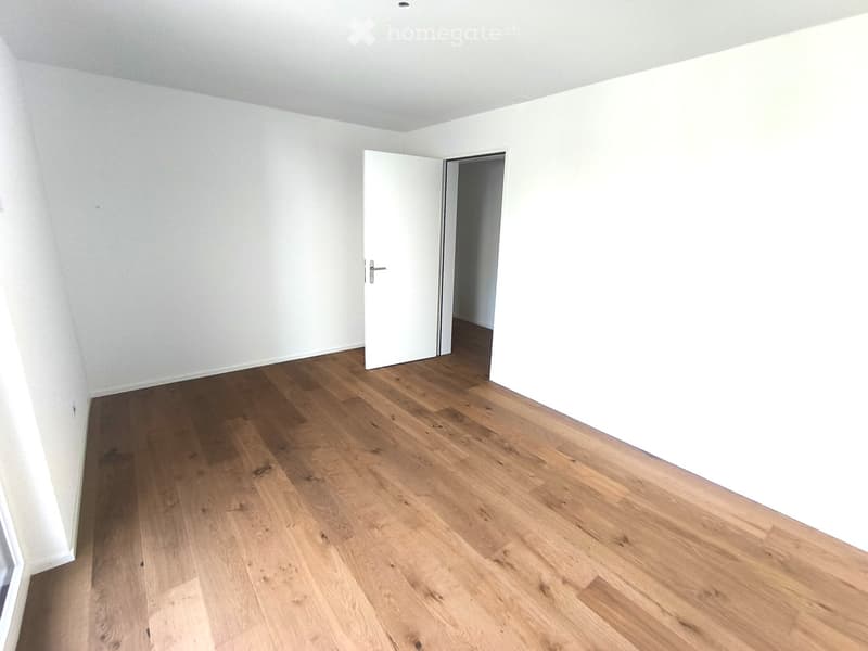 Empty room with light wooden flooring and white walls, featuring an open doorway leading to another space.