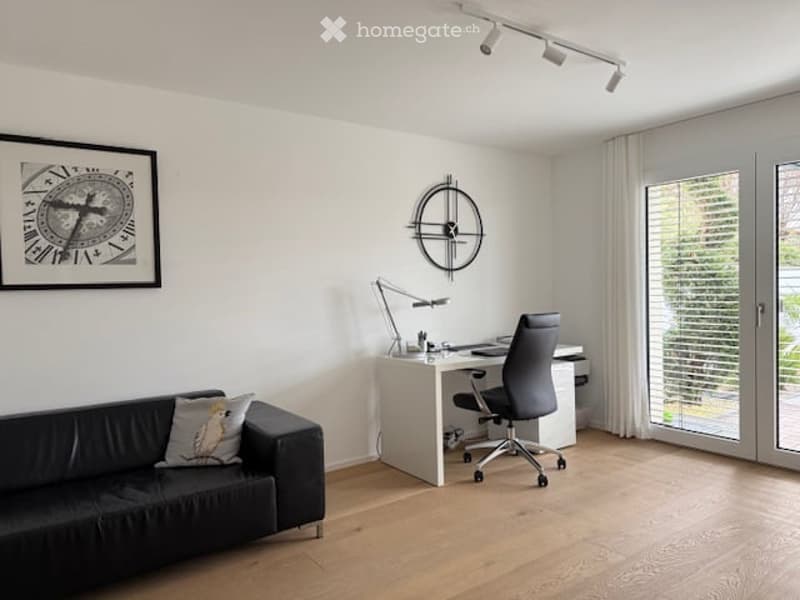 Modern, minimalist room with a black leather sofa, a white desk with a chair, a floor lamp, and a large picture frame on the wall.