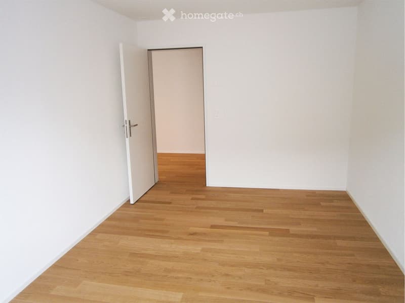 Empty room with white walls, wooden floor, open door leading to another room