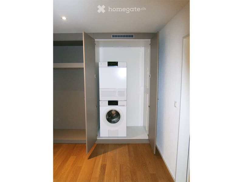 A small room with a washer and dryer, wooden floor, and white walls.