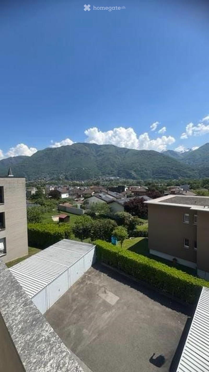 Balcony or terrace overlooking a residential area with houses, greenery, and distant mountains under a clear blue sky.