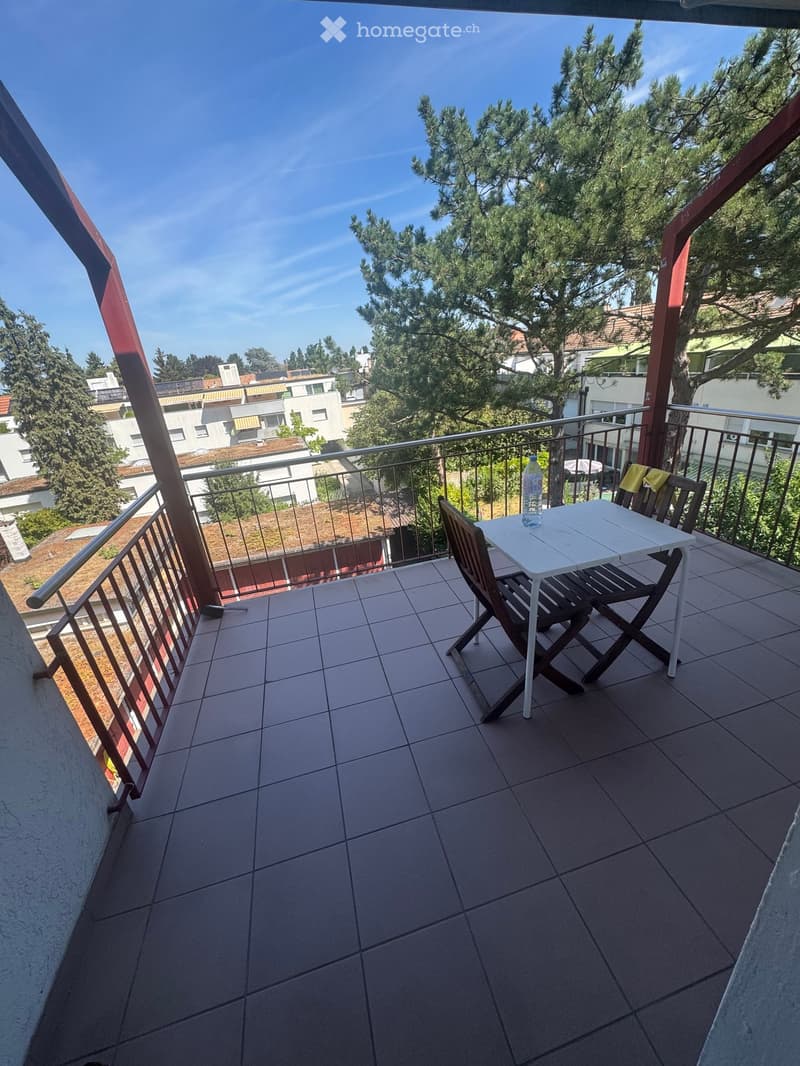 Balcony with tiled floor, metal railing, white table, wooden chairs, and a bottle on the table.