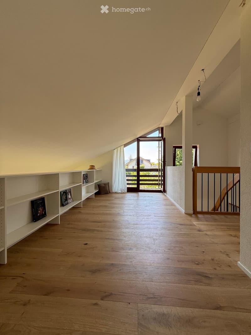 Bright, open hallway with wooden flooring, white walls, built-in shelving, and a staircase leading upwards.