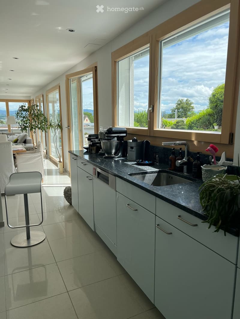 Modern kitchen with white cabinets, granite countertop, sink, mixer, coffee maker, and a stool near the window with a view.