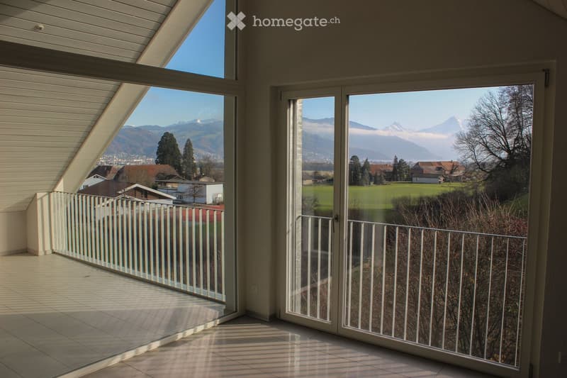 Bright balcony with large glass doors opening to a scenic view of mountains and countryside, featuring a white railing and tiled floor.