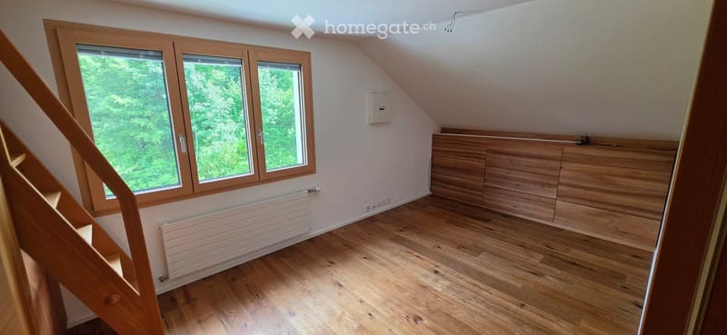 Empty attic room with wooden flooring, large windows, built-in wooden cabinetry, and a staircase leading up.