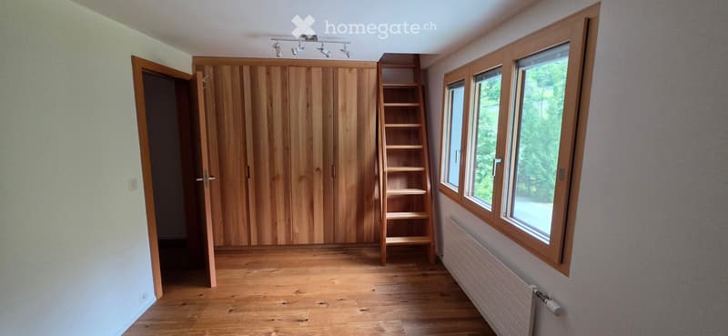 Empty room with wooden flooring, large wooden wardrobe, built-in shelving unit, and large windows with wooden frames.