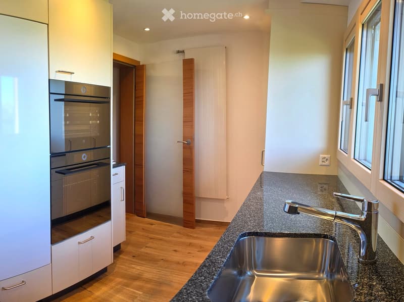 Modern kitchen with white cabinets, stainless steel sink, and built-in oven. Granite countertop and wooden flooring.