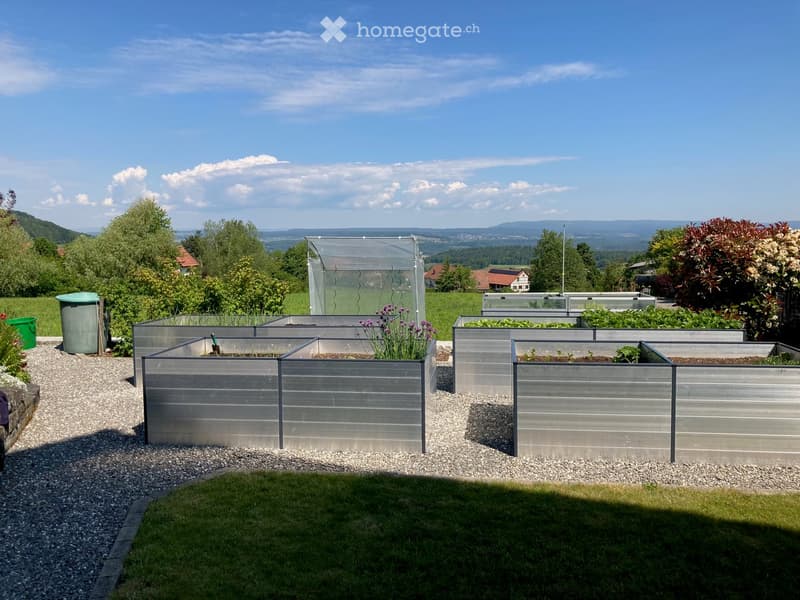 Well-maintained garden with raised metal planters, lush greenery, and a scenic mountain view in the background.
