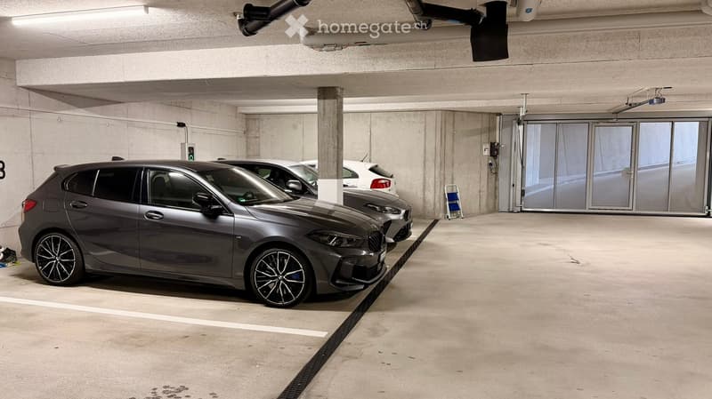 Underground parking area with several parked cars, concrete pillars, and a glass entrance door.